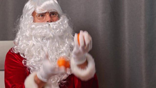 Santa Claus juggles three tangerines while sitting on a chair