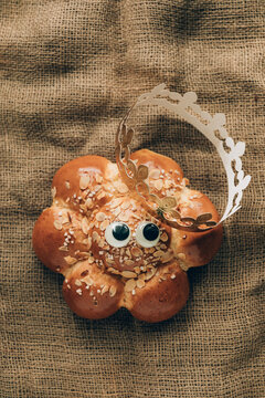 Three Kings Cake with a golden crown and a tiny king hidden inside. Swiss tradition to bake Dreik&ouml;nigskuchen on January 6. Rustic sackcloth background, funny googly eyes.