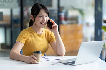 Attractive young Asian woman talking on the phone with some people. Students are calling their friends while doing their homework at home.