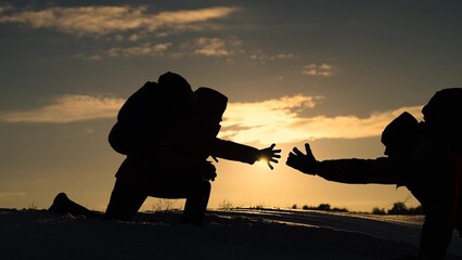 Silhouettes of climbers give each other helping hand, climbing to top of snowy mountain, hill....