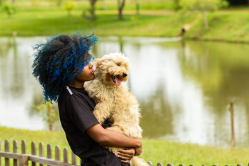 Uma jovem mulher, com cabelos afro pintados de azul, com um cachorro nos braços.