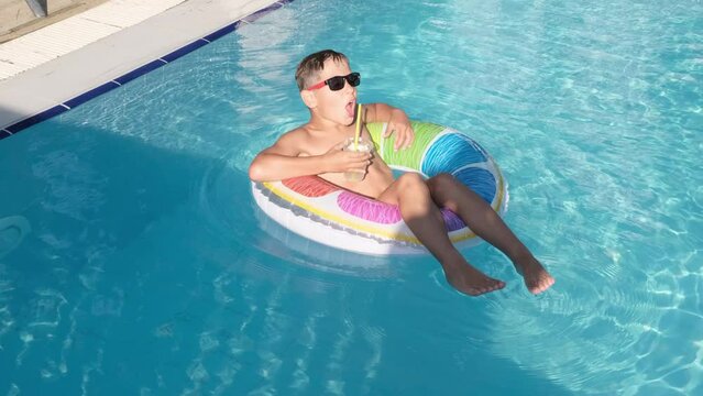 Embracing Summer Bliss: A young boy effortlessly floats on a pool float, savoring a refreshing cocktail. The epitome of leisure on a scorching day