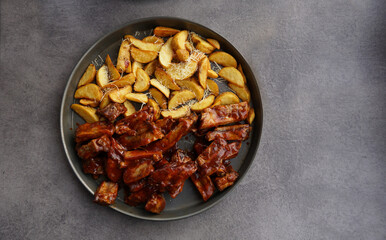 Tasty pork ribs with BBQ sauce and potato wedges with cheese served on metal plate. View from above, top. Copy space.