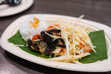 Spicy papaya salad with salted crab on paper dish.