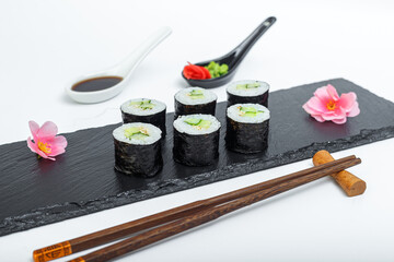 sushi with fresh cucumber, bowls and chopsticks, on a black plate, slate stand, on a white isolated background