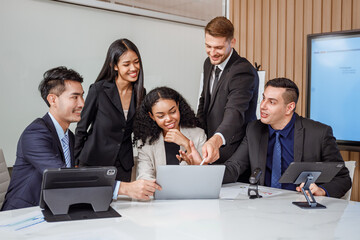 Team of business men and women looking at computers and celebrating successful business in conference room
