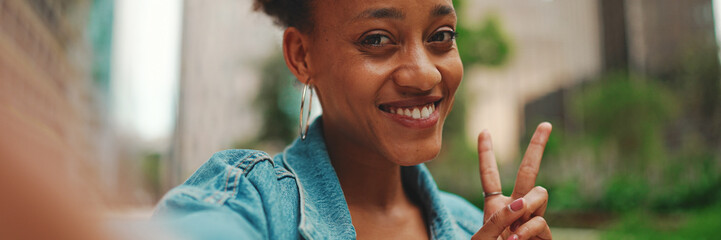 Closeup portret cute African girl with ponytail, wearing denim jacket makes stream, video call on smartphone in modern city background. © Andrii Nekrasov