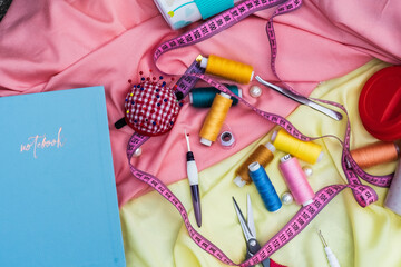 sewing accessories, pin cushion, blue notebook, pink measuring tape, spools of thread on yellow and...