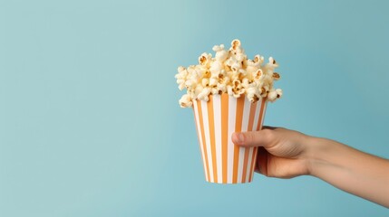 Hand holding striped bucket with popcorn on plain background