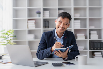 Fototapeta premium Handsome Asian businessman take notes and with laptop in the office.