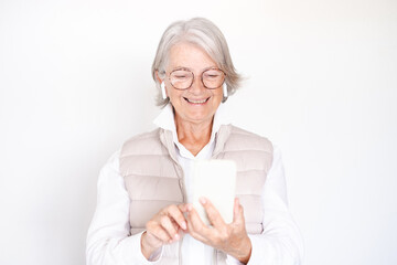 Smiling white haired senior woman with eyeglasses using mobile phone listening with earphones....
