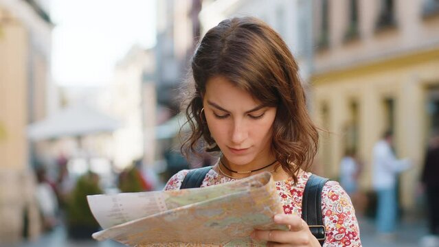 Caucasian young woman lost while traveling in Europe city, exploring sightseeing, navigating, looking way destination outdoors. Adult girl holding tourist paper map standing in street. Town lifestyles