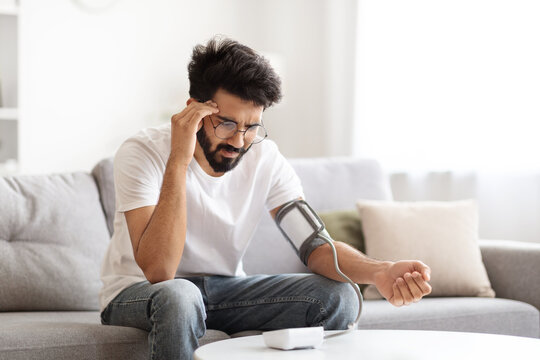 Sick Young Indian Man Checking Blood Pressure With Modern Tonometer At Home