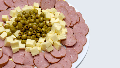 Cheese pieces, salami and pickled green olives on a round plate on white background. Top view, copy space.Plate of traditional smoked cold meat sliced ​​and bacon Isolated on white background