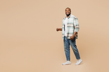 Fototapeta na wymiar Full body side profile view happy young man of African American ethnicity he wear light shirt casual clothes walking going stroll isolated on plain pastel beige background studio. Lifestyle concept.