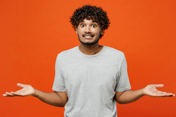 Young sad Indian man he wears t-shirt casual clothes spread hands shrugging shoulders looking...