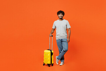 Full body traveler woman wears casual clothes holding suitcase isolated on plain orange red background studio. Tourist travel abroad in free spare time rest getaway. Air flight trip journey concept.