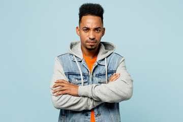 Fototapeta premium Young sad man of African American ethnicity in denim jacket orange t-shirt hold hands crossed folded look camera isolated on plain pastel light blue cyan background studio portrait Lifestyle concept