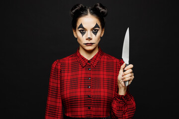 Young woman with Halloween makeup face art mask wearing clown costume red dress holding in hand knife look camera isolated on plain solid black background studio portrait. Scary holiday party concept.