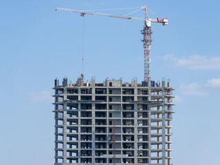 Fototapeta premium Industrial construction cranes work above new modern building. Engineering multistory design from concrete block and overlap. Development high-rise apartment with place for windows and balconys.