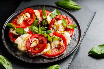 Italian caprese salad with mozzarella, tomatoes and basil on slate board. Plate of healthy classic delicious caprese salad on black plate