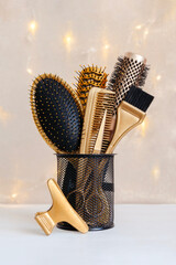 Hairdressing gold combs, brush and scissors in a stand. Accessories for a hair salon on the background of Christmas lights. - obrazy, fototapety, plakaty