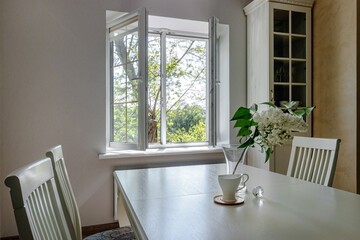 White bouquet of lilacs standing on a white table, against the background of the window