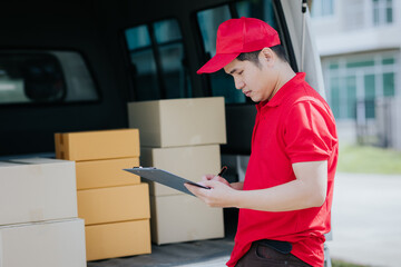 Young Asian woman receives a cardboard box from a smiling and happy delivery man at the front of...