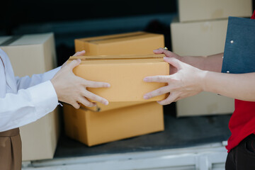 Young Asian woman receives a cardboard box from a smiling and happy delivery man at the front of the house. Asian male courier delivering goods to customers at doorstep