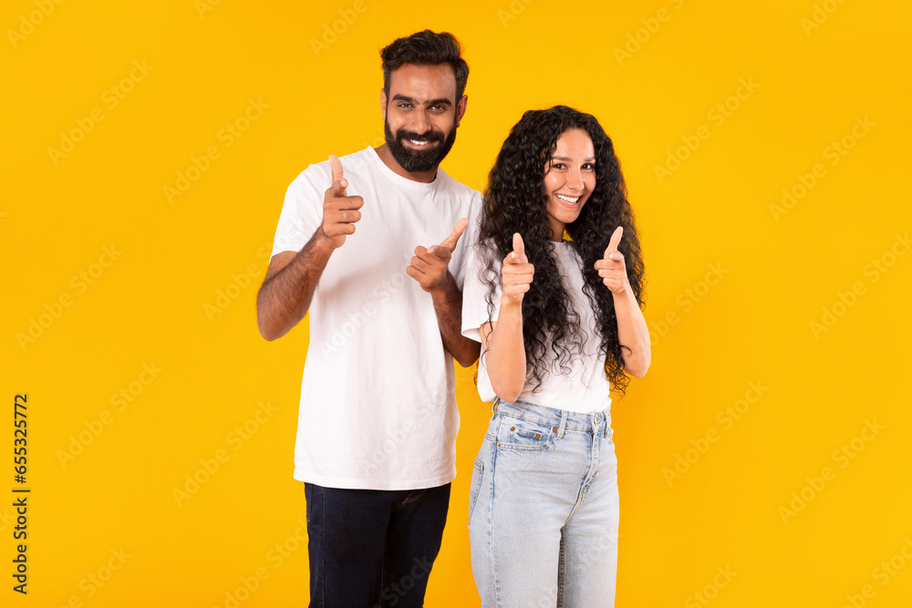 Wall mural middle eastern couple pointing fingers at camera over yellow background