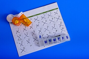 Prescription pill bottles weekly pill organizer opened to Sunday on calendar with days crossed off