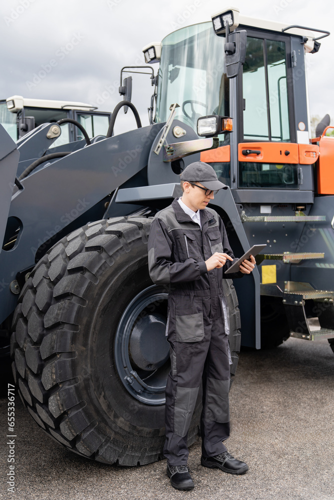Poster serviceman with digital tablet on a background of the tractor.