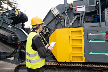 Engineer with digital tablet next to road construction machine - obrazy, fototapety, plakaty
