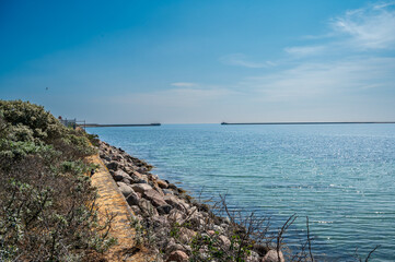 Fototapeta premium Blue sea with stone coast and pier in the distance
