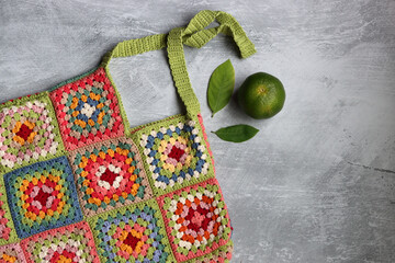 Handmade crocheted bag on grey textured background, top view. Close up photo of colorful crochet pattern. Eco friendly bag made of organic cotton yarn. Environment and plastic concept. 