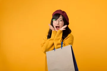 Fotobehang A fashion savvy individual, sporting a red beret and yellow sweater, exults in a shopping spree against a vibrant yellow background. © Jirawatfoto