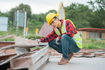 An engineer wearing a yellow hat, red shirt and green outerwear carries a radio at the construction site.