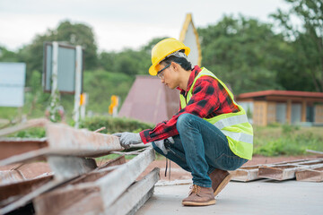 An engineer wearing a yellow hat, red shirt and green outerwear carries a radio at the construction site.