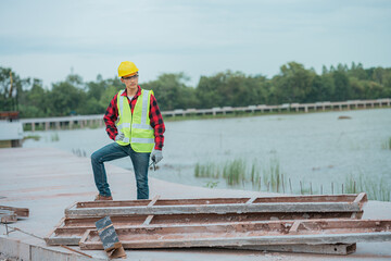 An engineer wearing a yellow hat, red shirt and green outerwear carries a radio at the construction site.