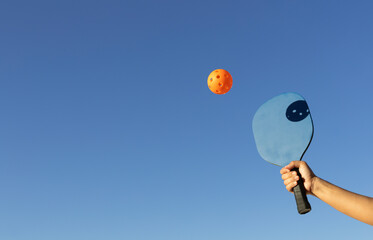 arm with pickleball paddle hitting orange ball