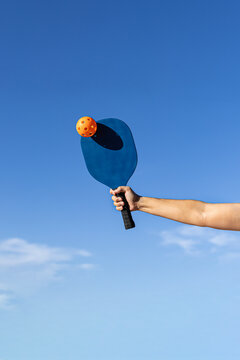 Arm with blue paddle hitting orange pickleball ball