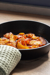 Fried pineapple in a cast iron frying pan. On a wooden chopping board in a kitchen