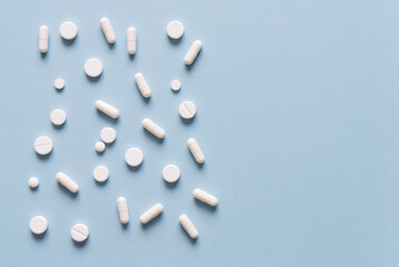  Scattered white pills on blue table. Mock up for special offers as advertising, web background or other ideas. Medical, pharmacy and healthcare concept. Copy space. Empty space for text or logo