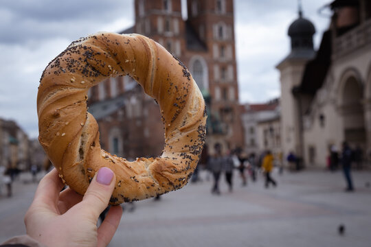 Tourist woman eating bagel obwarzanek traditional polish cuisine snack waling on Market square St. Mary's Basilica on the Krakow Main Square Rynek Glowny Poland. Krakow architecture, old city