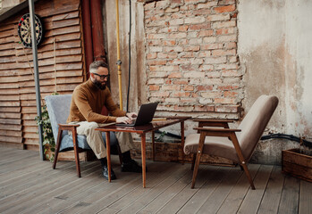 A stylish male freelancer is working on a new startup project, analyzing data using a laptop and a 5G wireless internet connection in a city cafe on a summer terrace with a free Wi-Fi zone