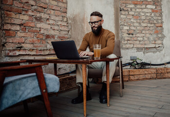 A stylish male freelancer is working on a new startup project, analyzing data using a laptop and a 5G wireless internet connection in a city cafe on a summer terrace with a free Wi-Fi zone - obrazy, fototapety, plakaty