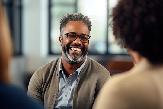 Group therapy and support. The focus is on a middle aged African American man in eyeglasses. A group of people around support him. He is happy.