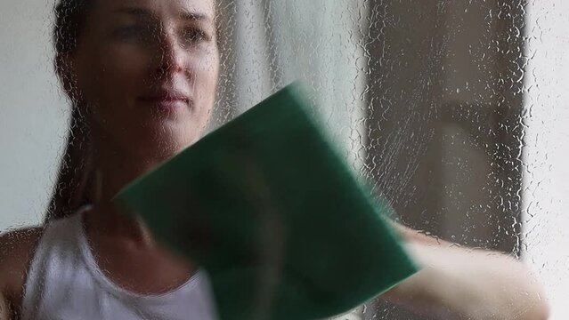 Young woman doing housekeeping, cleaning the window.