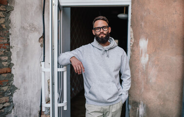 Urban Portrait of Handsome Hipster Man with a Beard Wearing a Gray Blank Hoodie with Space for your Logo or Design. Unique Mockup for Print