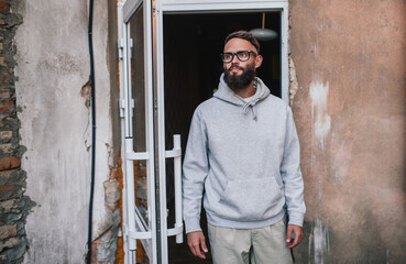 Urban Portrait of Handsome Hipster Man with a Beard Wearing a Gray Blank Hoodie with Space for your Logo or Design. Unique Mockup for Print